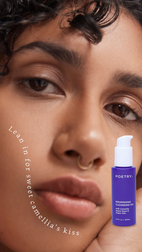 Woman with curly brown hair, brown eyes, brown skin, nose ring, lips closed staring at the camera with writing on her left face cheek that says Lean in for sweet camellia's skiss. For POETRY Skincare.